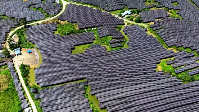Cinematic aerial: Drone descending over countryside with solar panels dotting fields alongside winding creek and village groves