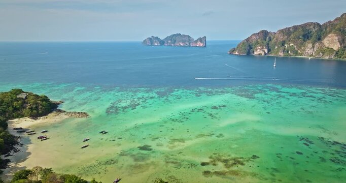 Koh Phi Phi Islands aerial landscape. Andaman Sea coastline with lush tropical rainforest, white sand beach, crystal clear turquoise water, long tail boats, and distant limestone karsts. Drone flight