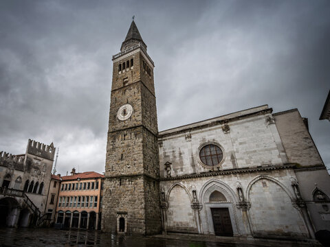 View of Titov trg square with the Cathedral of the Assumption, Mestni Stolp city tower and Praetorian Palace under dramatic clouds in the historic center of the Istrian town of Koper, Slovenia.