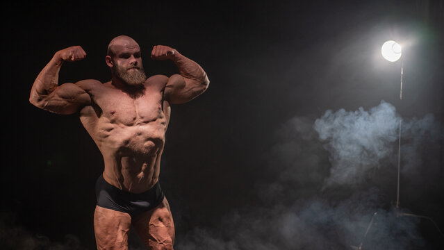 A male bodybuilder poses in shorts, showing off his muscles. 