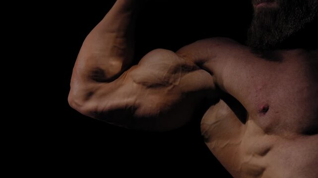A male bodybuilder poses in shorts, showing off his arm muscles.