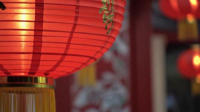 A close-up view of a glowing red Chinese lantern with yellow tassels hanging outdoors during a festive celebration.