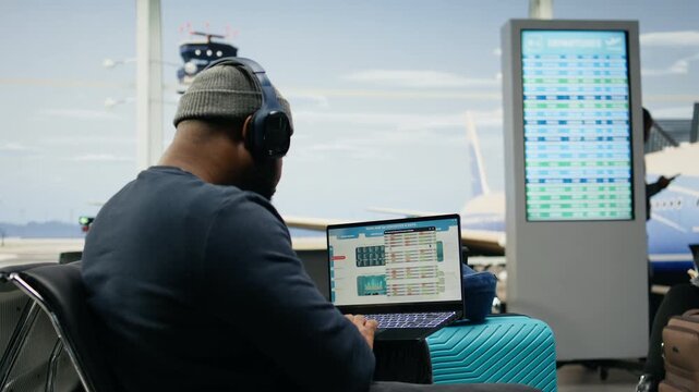 Black casual worker reviews insights and analytics on a laptop in an airport lounge, evaluating business performance and financial forecasts before a global company meeting during business travel.