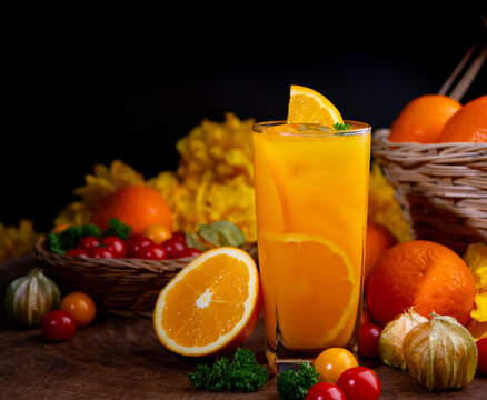 Glass of organic orange juice surrounded by fresh fruits and vegetables on dark wooden background, healthy drink concept