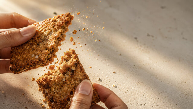 Crunchy cracker breaking in hands with crumbs flying in warm daylight, capturing satisfying snack moment full of texture and detail