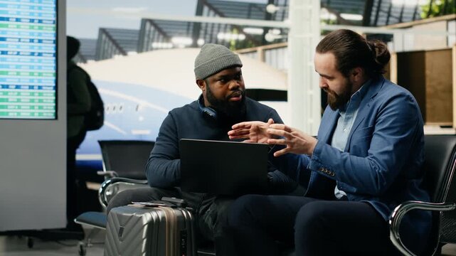 A manager and assistant use a laptop at the airport while preparing for a meeting abroad and a multinational company event at headquarters.