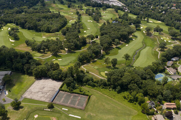Fototapeta premium Aerial drone view of golf course fairways, nearby homes, and mature trees in Bayberry Park, New Rochelle, New York