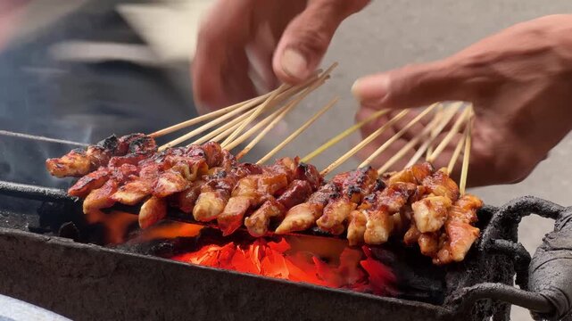 Hands Grilling Indonesian Chicken Satay Skewers on Hot Charcoal Fire