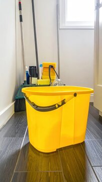 Bright yellow bucket and cleaning supplies next to a door, on a tiled floor