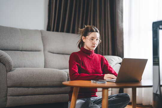 Asian woman using laptop on side table remote work from home for the holidays relax sitting in cozy living room