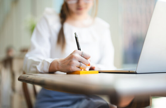 Closeup hand young adult  business woman using pen writing note for study, work online workplace cafe table with lapto