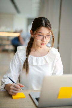 Young adult  business woman using pen writing note for study, work online workplace cafe table with lapto
