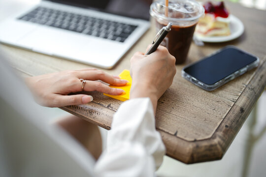 Closeup hand young adult  business woman using pen writing note for study, work online workplace cafe table with lapto