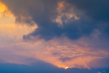 Obraz premium Dramatic sunset clouds with the sun disappearing behind the horizon. Natural background with golden, blue and purple tones for design and weather concepts.