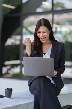 Asian businesswoman celebrating success working on laptop outdoor