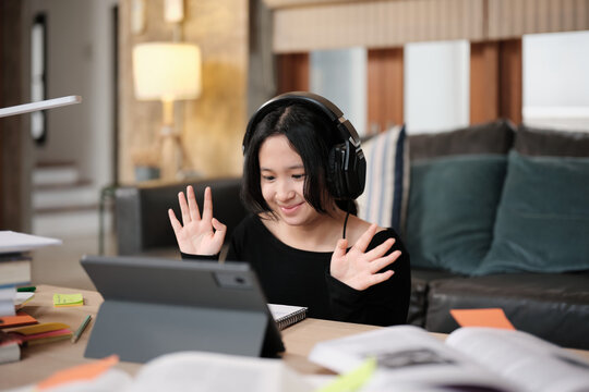 Asian teenage girl greeting in online class, remote learning at home using digital tablet, writing and reading textbooks, self-study for back to school, Homeschooling, university education lifestyle.