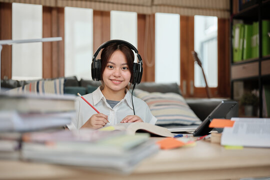 Portrait of Asian teenage girl, cheerful learning at home, reading textbooks, note writing, self-tutorial exam, Homeschooling, university knowledge education lifestyle, smiling and looking at camera.
