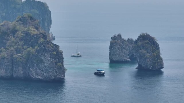 Koh Lanta seascape with boats navigating the clear turquoise waters of the Andaman Sea, surrounded by dramatic limestone karst islands covered in lush tropical vegetation. Aerial drone shot panorama