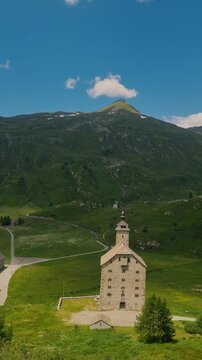 The iconic Old Hospice (Alter Spittel) at Simplon Pass, Switzerland, stands proudly in a lush alpine landscape with green meadows and spectacular summer mountain views, vertical shot