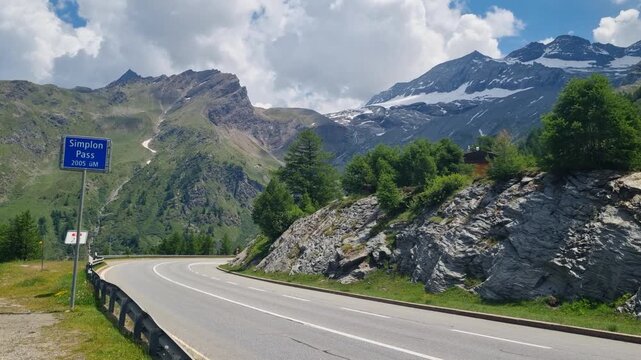 Empty Simplon Pass road in Valais, Switzerland, featuring the official street sign and dramatic alpine scenery. A peaceful European mountain route crossing the Alps between Switzerland and Italy