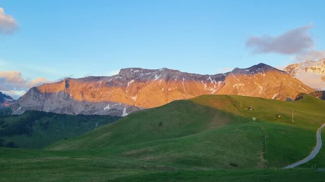 Serene sunset over Hahnenmoos Pass in the Bernese Alps, Switzerland. Warm evening light highlights majestic mountains, lush green summer meadows, and a peaceful alpine landscape