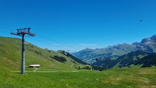 Panoramic view with Hahnenmoos gondola lift in Adelboden, Switzerland, overlooking lush green alpine meadows and the majestic Bernese Oberland Alps under a bright sunny sky