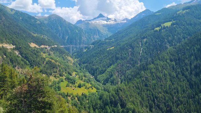 Scenic view of Simplon Pass, Switzerland, with forested Alpine mountains and the Ganter Bridge in Ganter Valley visible beneath a clear blue sky, Swiss road trip destination and stunning landscape