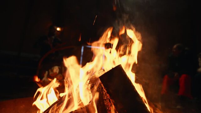 Bright campfire flames rising from stacked logs during outdoor winter night, slow motion