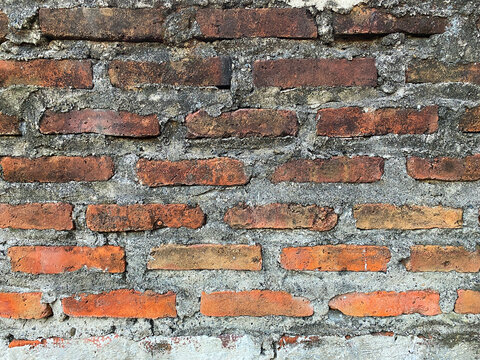 Full frame background of a vintage unplastered red brick wall texture with rough cement mortar layers between the bricks.