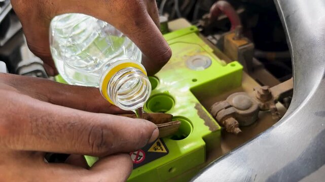 Mechanic Refilling Car Battery Cells With Distilled Water During Vehicle Maintenance