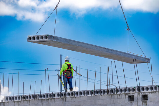 Low angle view of a construction worker guiding a precast hollow core concrete slab lifted by a crane at a building site