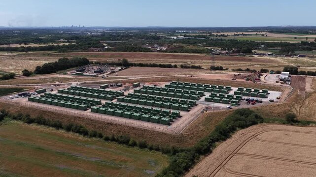 Extensive industrial battery energy storage system facility filmed from an aerial perspective, showcasing rows of green containerized units designed for renewable power grid stability