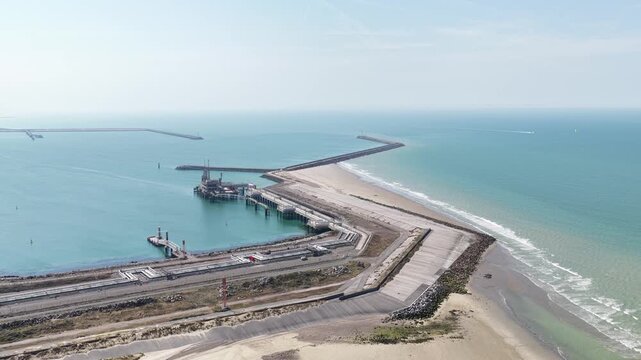 Expansive aerial footage showcasing a large industrial port with a liquefied natural gas terminal, extensive breakwaters, and calm turquoise ocean waters under a clear sky on a sunny day