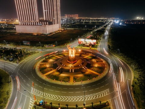 Kosambi, Banten, Indonesia - 18 October 2025: Aerial view of the illuminated Monumen Bung Karno - Bung Hatta PIK2 at a roundabout at night, with light trails and high-rise buildings.