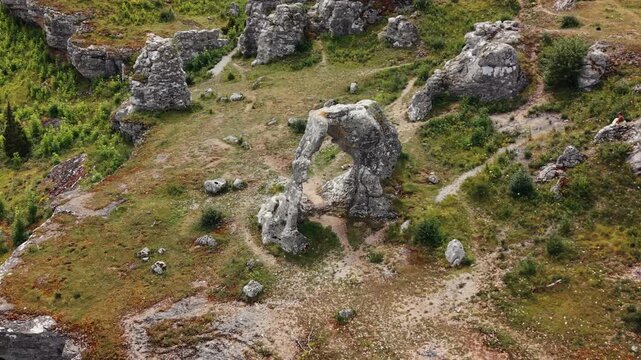 Aerial view of weathered limestone rauks and a natural rock arch at Lergrav on Gotland, revealing erosion-shaped geology, footpaths and sparse vegetation.