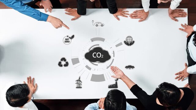A diverse group of professionals engages in a dynamic discussion around a table, focusing on strategies for achieving net zero carbon emissions and implementing sustainable practices. Raster