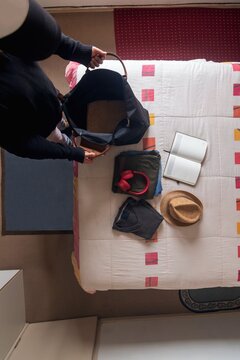 Top view flat lay of a man packing a travel bag on a bed with clothes, headphones, and a hat