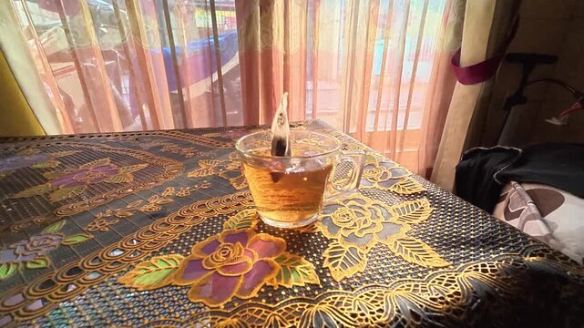 GRESIK, INDONESIA - JULY 30, 2026: Putting a tea bag into a glass of hot water to brew tea during morning routine.