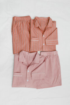 Top view of two striped pink red pajama suits on white bed. Minimal style, cozy, comfort pyjamas. Sleepwear fashion concepts, self-care, wellness, calm lifestyle, home aesthetics, morning routines