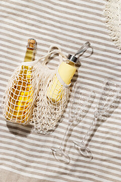 Summer lifestyle outdoor scene, bottle of white sparkling wine and cold water, two glasses, sun hat, sun shadows. Romance beach rest, weekend or picnic, travel holiday concepts, yellow beige colored.