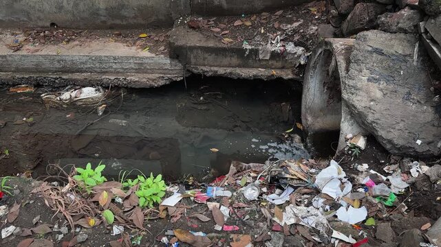 Static shot of a polluted roadside storm drain clogged with plastic litter and stagnant water highlighting urban waste management and environmental pollution