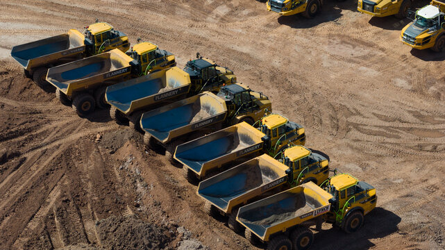 Birmingham, England, United Kingdom - 12 July 2026: Aerial view of a line of yellow articulated dump trucks parked on a muddy construction site.