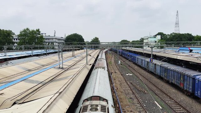 wide angle shot of a passenger train departing from a railway platform with parallel freight tracks and overhead power lines