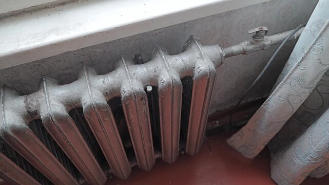 Aged cast iron radiator beneath a window highlights classic indoor heating design.