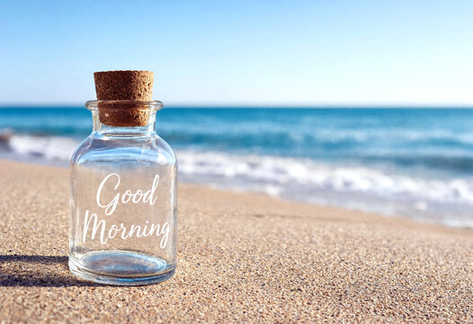Small glass bottle with good morning message on sandy beach with ocean waves in background