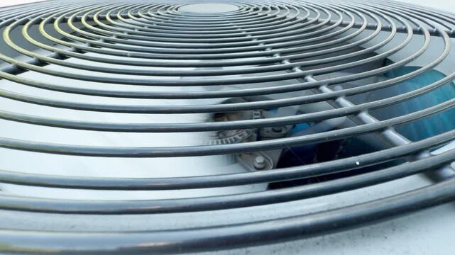 A large fan spins rapidly inside an outdoor ventilation unit. This heavy cooling system creates the constant hum of an industrial air conditioner.