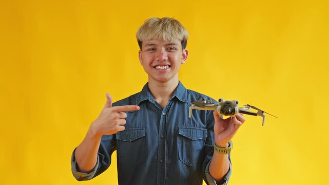Happy young man pointing at compact drone in hand against bright yellow background
