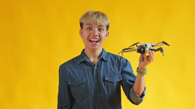 Excited young Asian man displaying compact drone against vibrant yellow background