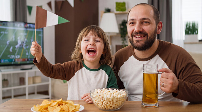 Toddler waves flag while father watches football gameday on television at home with popcorn chips beer for party fun