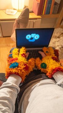 POV of a person wearing fuzzy monster gloves typing on a laptop in a cozy home environment